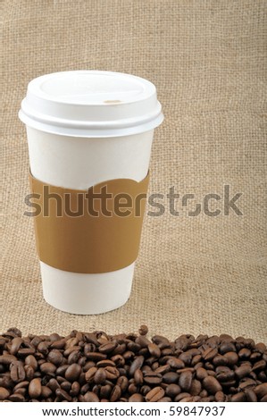 Paper coffee cup with safety cardboard collar on jute background with coffee beans and copy space.