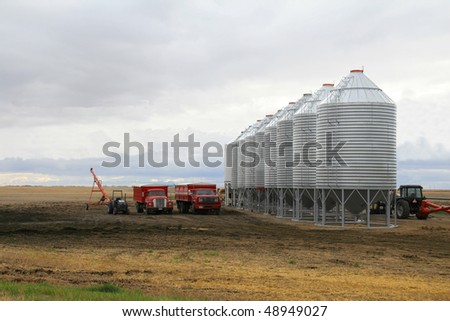 row of steel grain bins dwarfing grain trucks and tractors