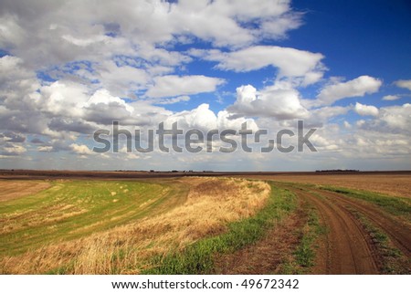 Rural Dirt Road alongside harvested grain field under dramatic prairie sky