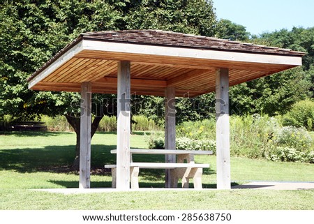 Roadside rest area with a picnic table and trees in background. There is a cover or canopy over the picnic table.