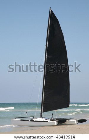 Catamaran with black sail at the beach