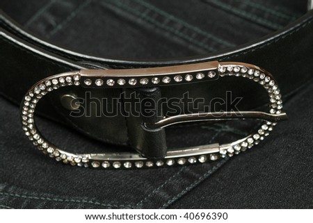 Closeup of silver belt buckle studded with diamonds crystals on jeans background. Luxury and casual