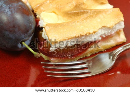 Closeup of the plum cake with fresh plum and fork on red plate. Autumn cake with meringue