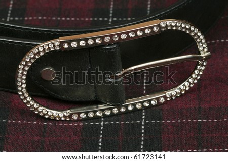 Closeup of silver belt buckle studded with crystals on chequered wool fabric. Luxury and casual fashion