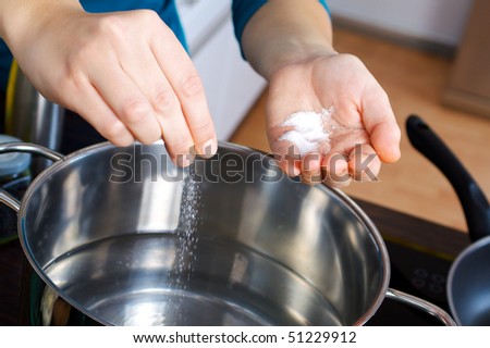 Woman salting water in a pot on a stove in the kitchen