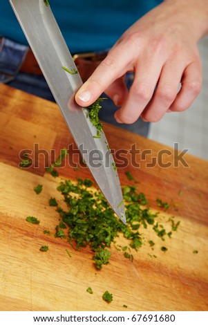 Woman hackles parsley with a big knife on cutting board