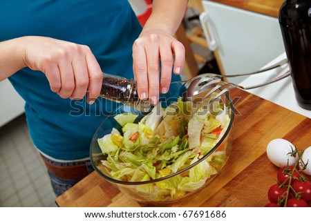 Woman seasoning salad with black pepper from a mill