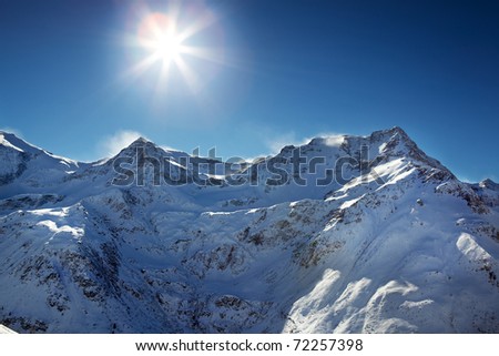 Sun glares at the sky over alp mountains with blizzard