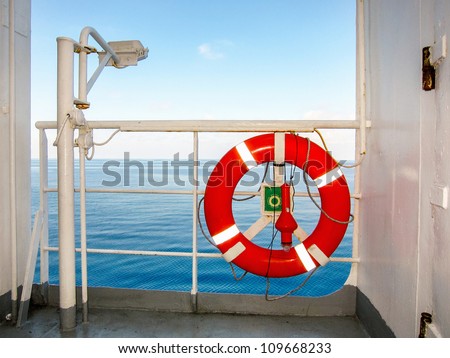 Red life buoy or preserver mounted on the rail of a passenger liner to be thrown overboard as a flotation device in case of drowning