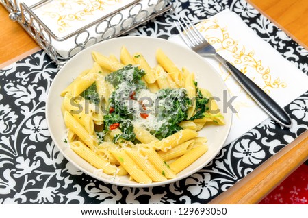 Elegant table setting with dinner for one consisting of a bowl of penne pasta with spinach and parmesan cheese