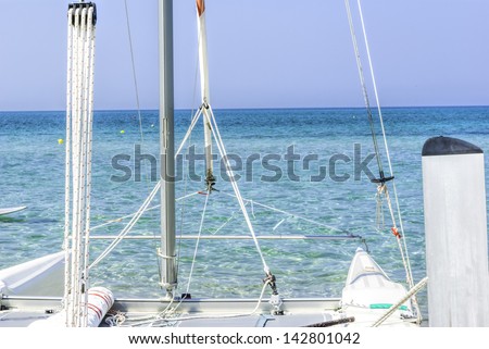 Closeup of a moored white catamaran sailboat against a calm blue tropical ocean under summer sunshine