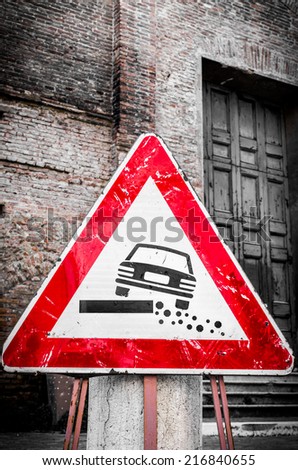 Triangular traffic warning sign propped up in front of an old brick building for damaged road edges or shoulders showing a car at a tilted angle