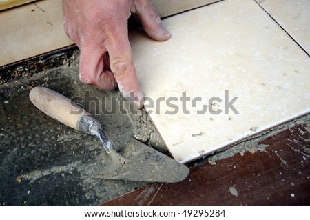 Detail of mason tiler hand laying a tile on the floor