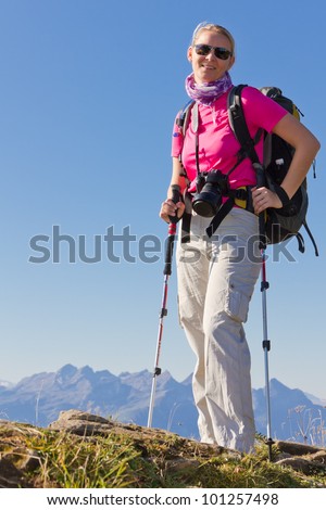 woman hiking in high mountains with sunglasses walking sticks, backpack and camera, Switzerland