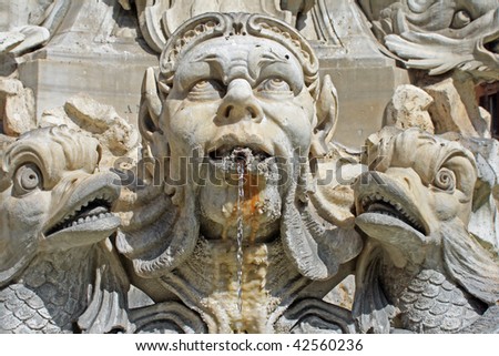 fountain with a male male head spitting water gazing to the sky and a fish figure on each side
