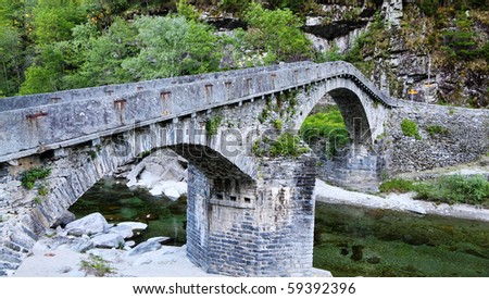 historic curved stone bridge built of rough gray stone crossing a mountain stream