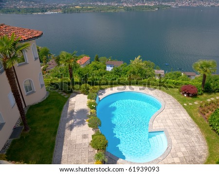 mansion like house with round tower and palm tree an pool resides high over a lake