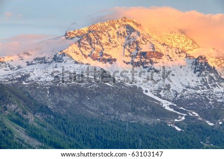 view from St. Moritz in Switzerland: high snow and ice capped alpine mountain range with red illuminated peaks at sunset