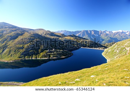 calm, dark cold mountain lake surrounded by rocky alpine mountain ranges and blue sky