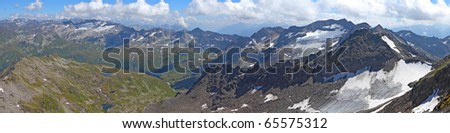 long mountain panorama in summer of the view from Gemsstock mountain above Andermatt in summer seen below in Switzerland with grassy mountains in the front and white mountains behind