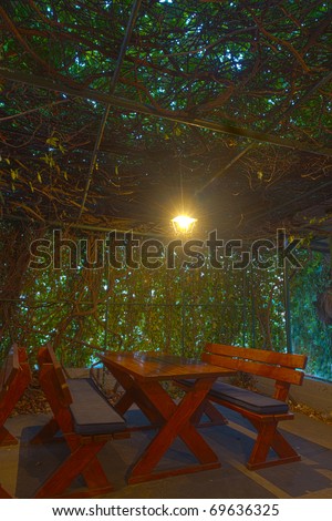 rustic romantic dimly lit wooden sitting group consisting of table and two benches under a vine overgrown pergola