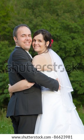 newly wed couple with wedding gown and dark suit: groom and bride hand in hand proud and happy looking over the shoulder