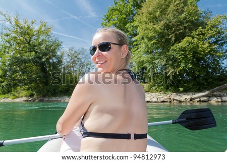 pretty young woman sits in boat paddle in hand on a river in pretty natural summer settings
