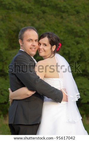 newly wed couple with wedding gown and dark suit: groom and bride hand in hand proud and happy looking over the shoulder