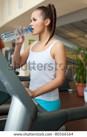 beautiful girl drinking water from a bottle after a workout at the gym on the treadmill