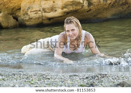 redheaded girl in a wet white T-shirt sitting in the water and playing with mud
