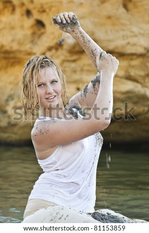 redheaded girl in a wet white T-shirt sitting in the water and playing with mud