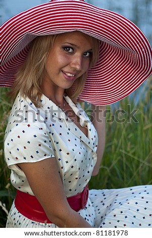 beautiful girl in a pink hat and white dress with red belt walking in the park