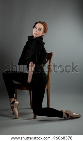 young ballerina performs exercises near the chair