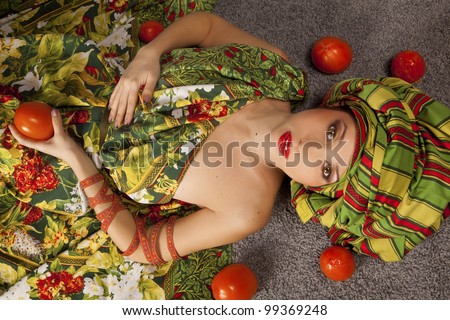 young woman in a green luxurious dress, green hat. holds red tomatoes lying on the floor