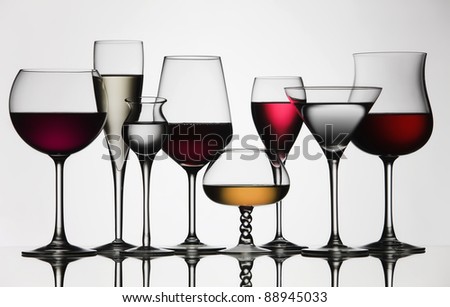 Eight difference glasses of wine and spirit, on a mirror and white background.