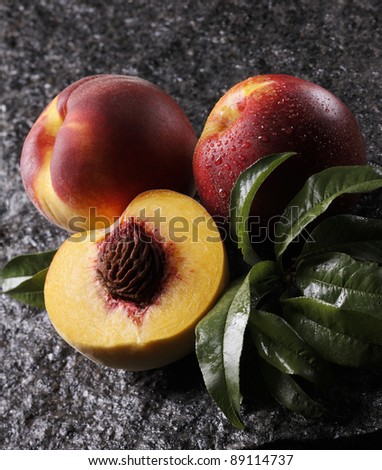 Three wet peaches, one cut in half, with leaves on a wet stone