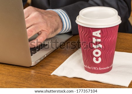 MILTON KEYNES, England - FEBRUARY 14, 2014: A cup of Costa coffee in front of a business man working on a laptop computer.