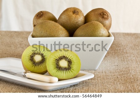 Kiwi fruits in a dish with one cut in half. Focus is on the cut fruit.