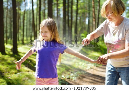 Middle age woman applying insect repellent to her granddaughter before forest hike beautiful summer day. Protecting children from biting insects at summer. Active leisure with kids.