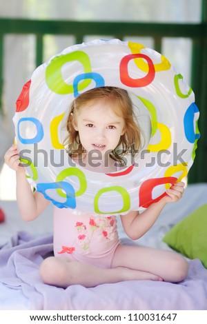 Cute little girl in swimsuit looking through a swim ring