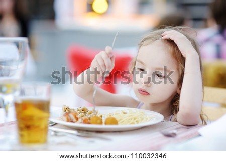 Cute little girl eating spaghetti outdoors