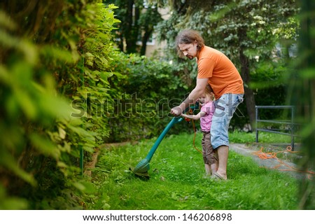 Father and a child cutting the grass with a lawn trimmer