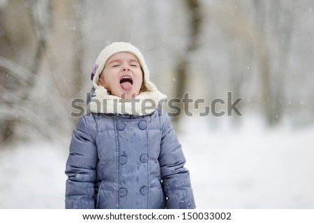 Adorable little girl catching snowflakes with her tongue