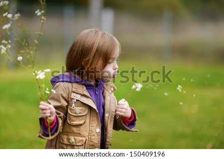 Adorable girl blowing off dandelion on late autumn day