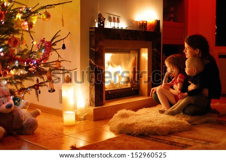 Young Mother And Her Daughters By A Fireplace On Christmas