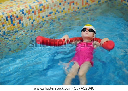Happy little girl learning to swim with pool noodle
