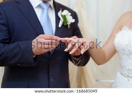 Groom is putting the wedding ring on bride\'s finger
