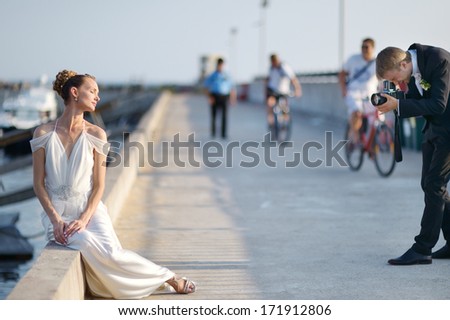 Bride posing while her groom is shooting with an old camera