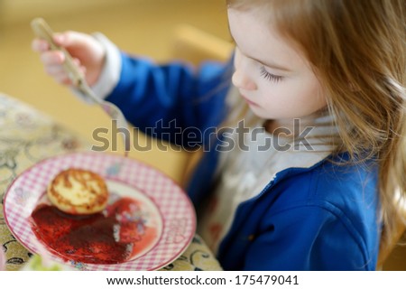 Cute little girl eating pancakes with jam outdoors