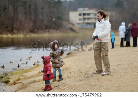 Father and his daughters feeding ducks at autumn